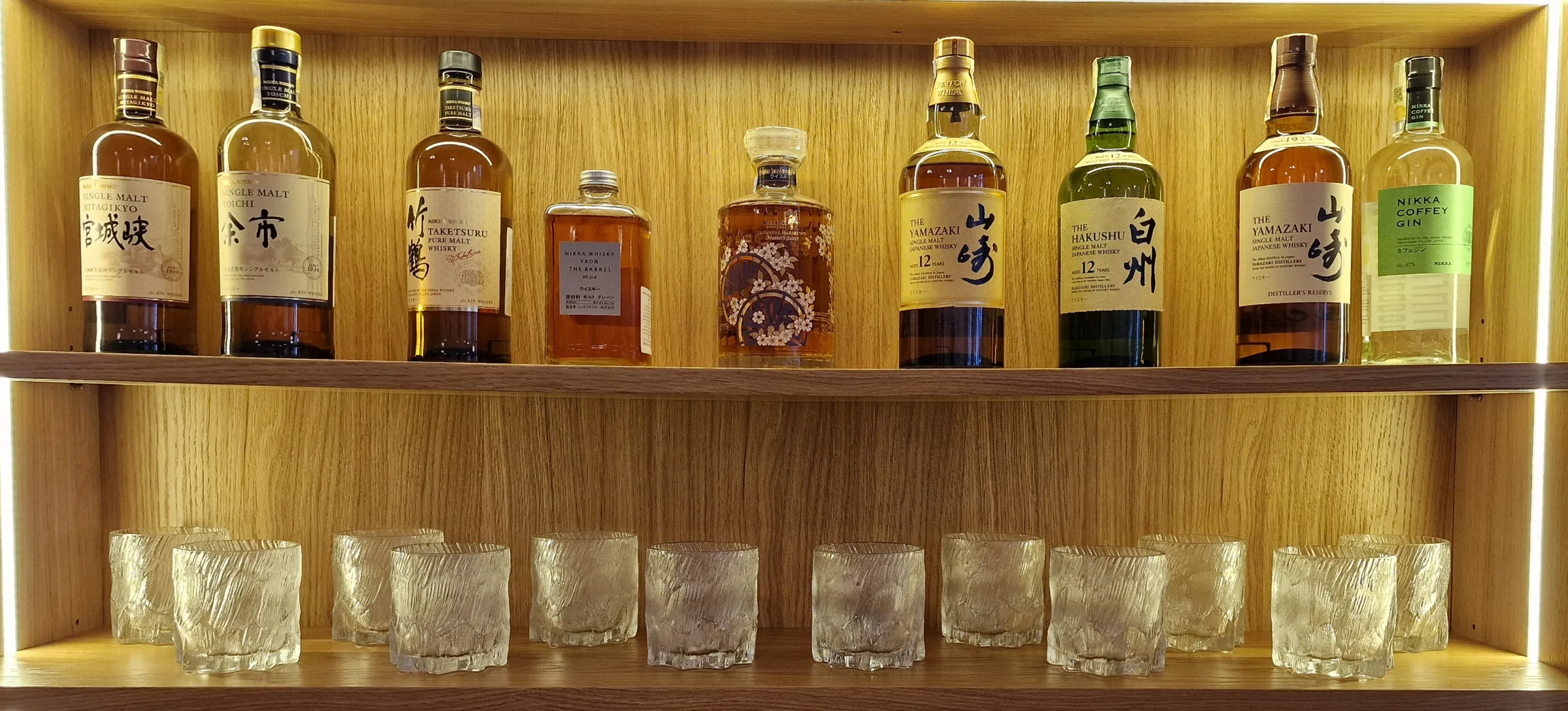 _Image_1hylna1hylna1hyl (1) kopie wisky Na obrázku je krásná sbírka prémiových japonských whisky, které jsou vystavené na podsvícené dřevěné polici. Skvěle to doplňuje luxusní atmosféru japonské restaurace Yamate